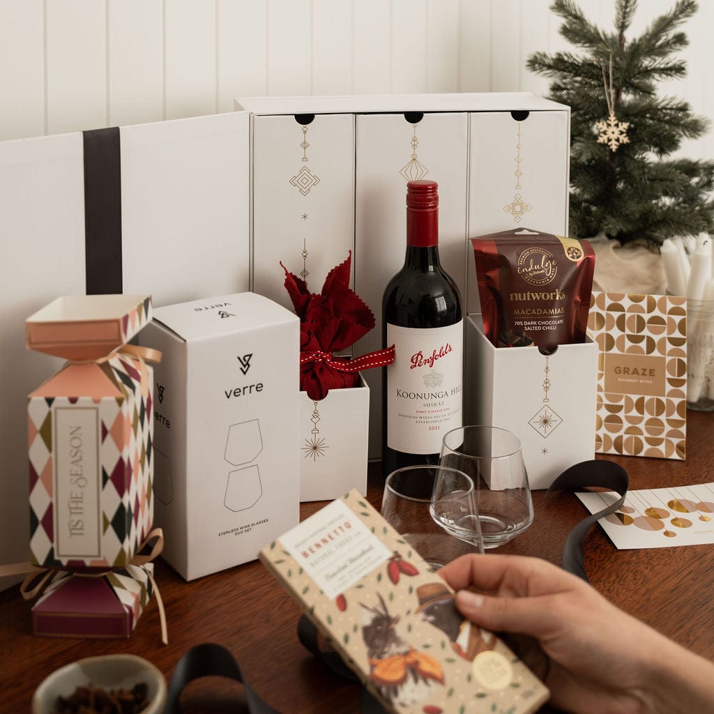 hand holding chocolate as part of advent gift that includes wine bottle, bon bon and glasses