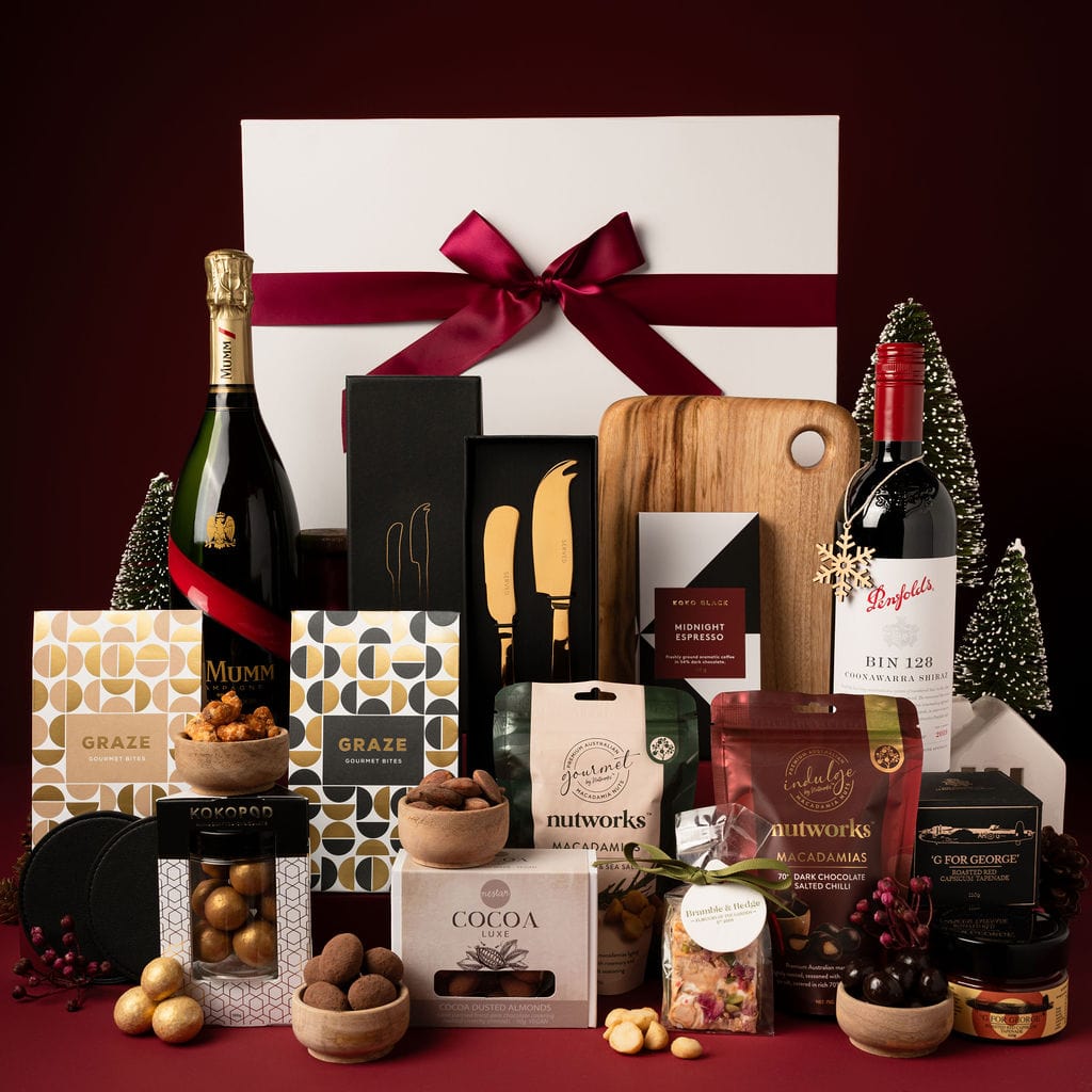 Large white gift box with red ribbon on display next to contents including mumm champagne, red wine, wooden board, nuts and chocolate