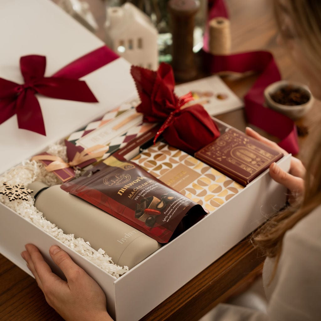 woman opening red christmas gift showing contents, bottle , nuts, pudding and snowflake decoration