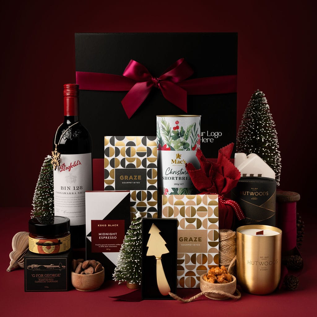 black gift box with contents on display including red wine, chocolate, shortbread and gold candle against red background