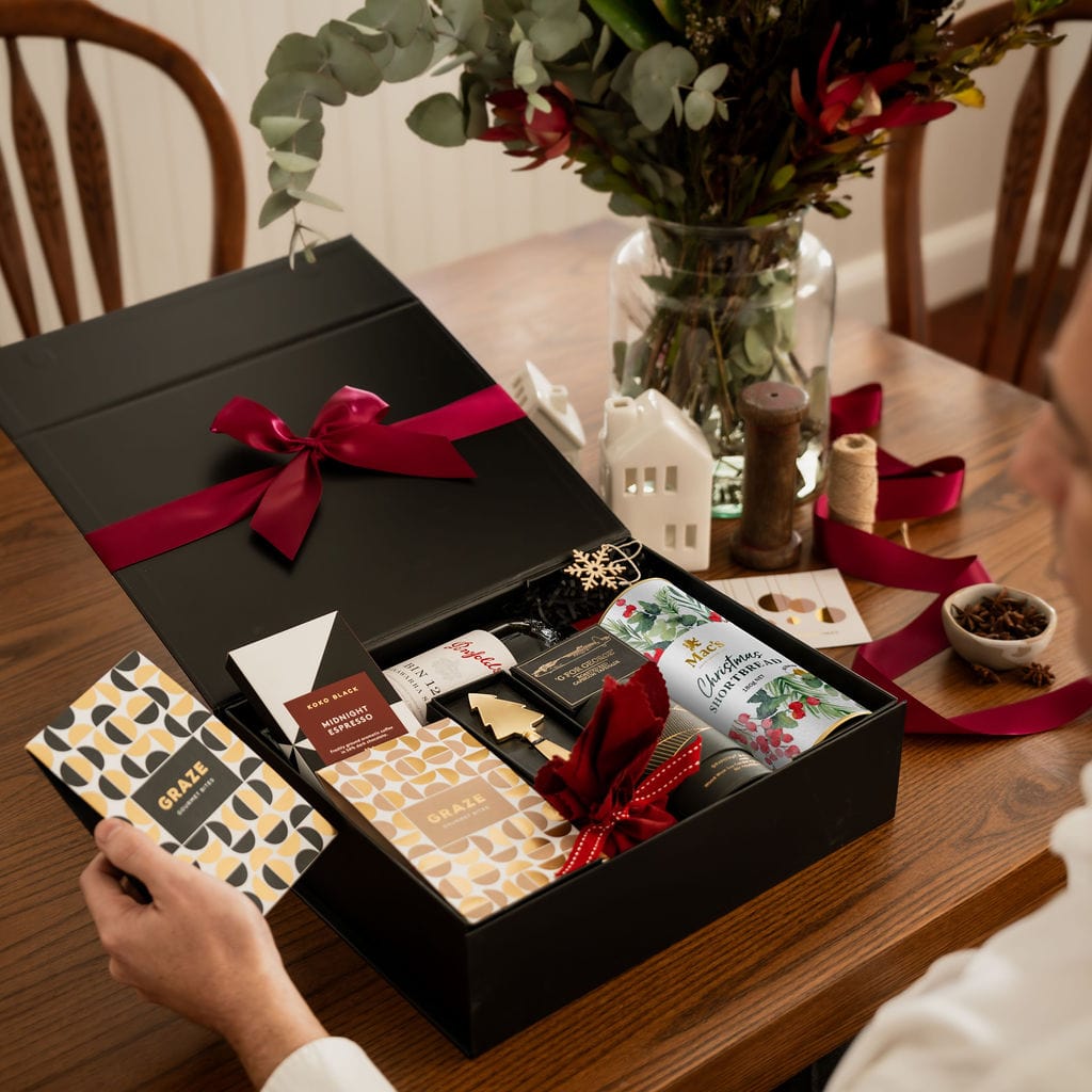 man holding black and gold packaged nuts as part of black gift box open on wooden dining table
