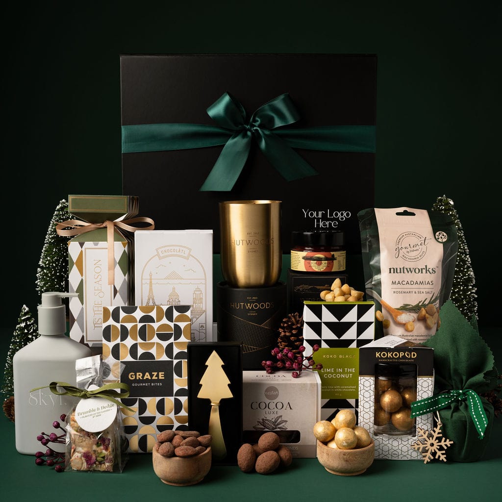 black gift box with contents on display to show candle, soap, nuts, chocolate, gold knife and pudding against green background