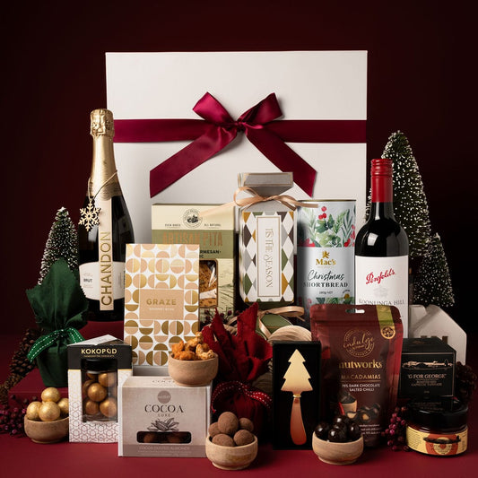 gift box with red ribbon on display next to contents, including champagne, red wine, chocolate, nuts and puddings 