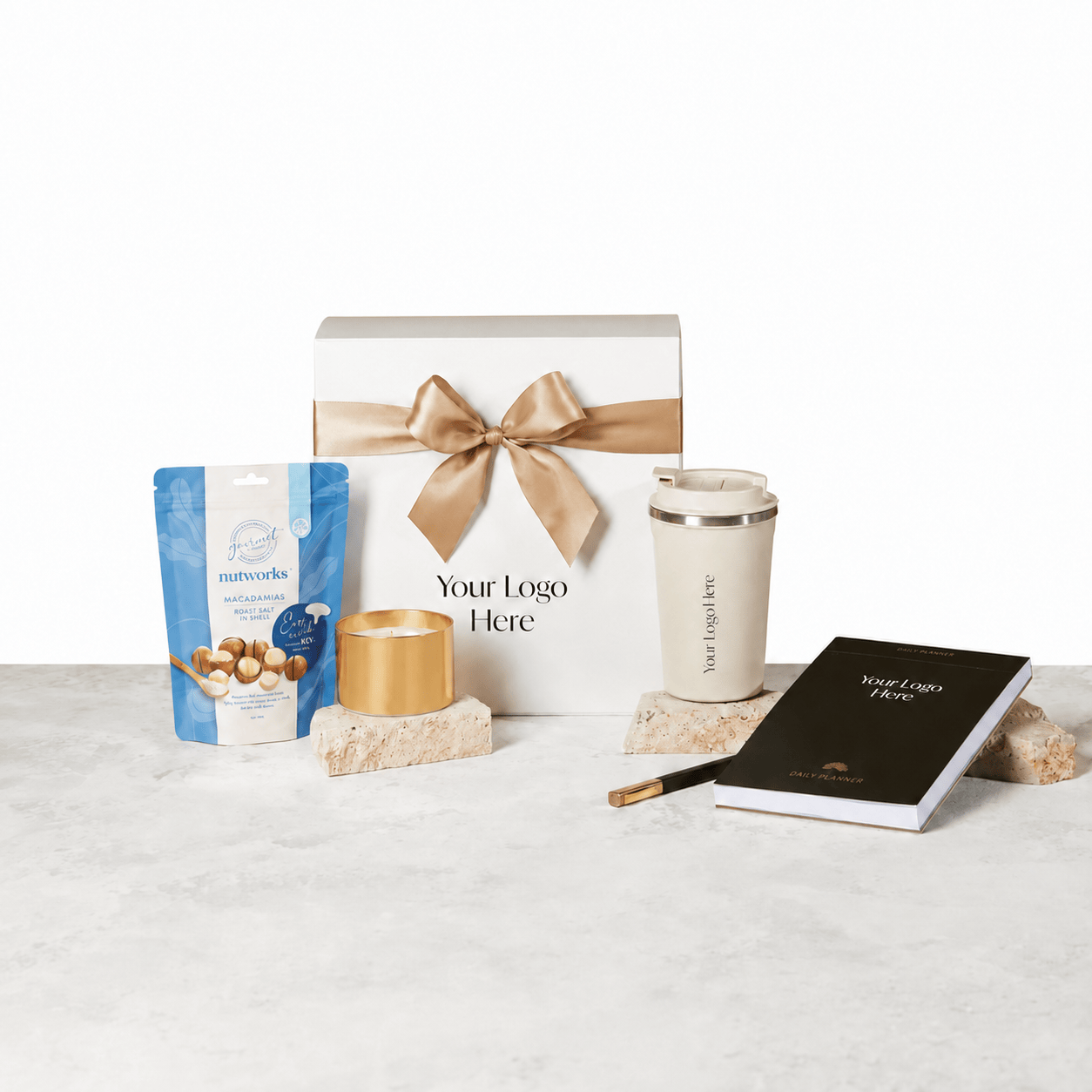 Finding Focus gift box with a tan ribbon and logo placeholder, shown with a Nutworks macadamias pouch, a Horizon brushed gold candle, a beige insulated keep cup and a black daily planner with pen on a light stone surface