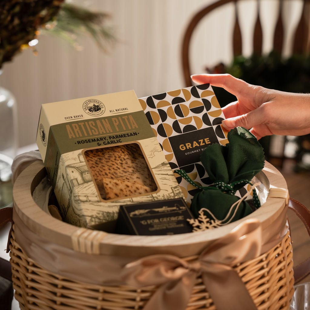 hand reaching for black and gold packaged nuts inside wicker basket gift