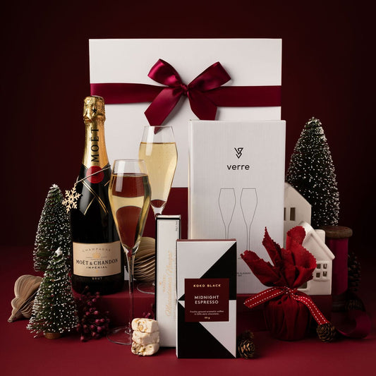 christmas gift box with champagne, glasses, chocolate and pudding on display against red back drop