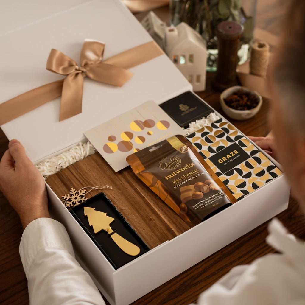 man holding open gift showing content of chocolate, wooden board and gold christmas tree knife