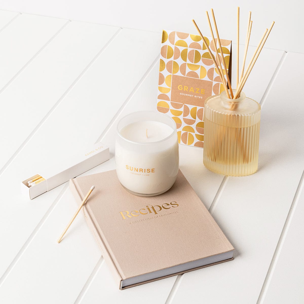 The reset gift box in light pink tones, with a reed diffuser, soy candle, recipe journal, long matches and graze gourmet bites. 