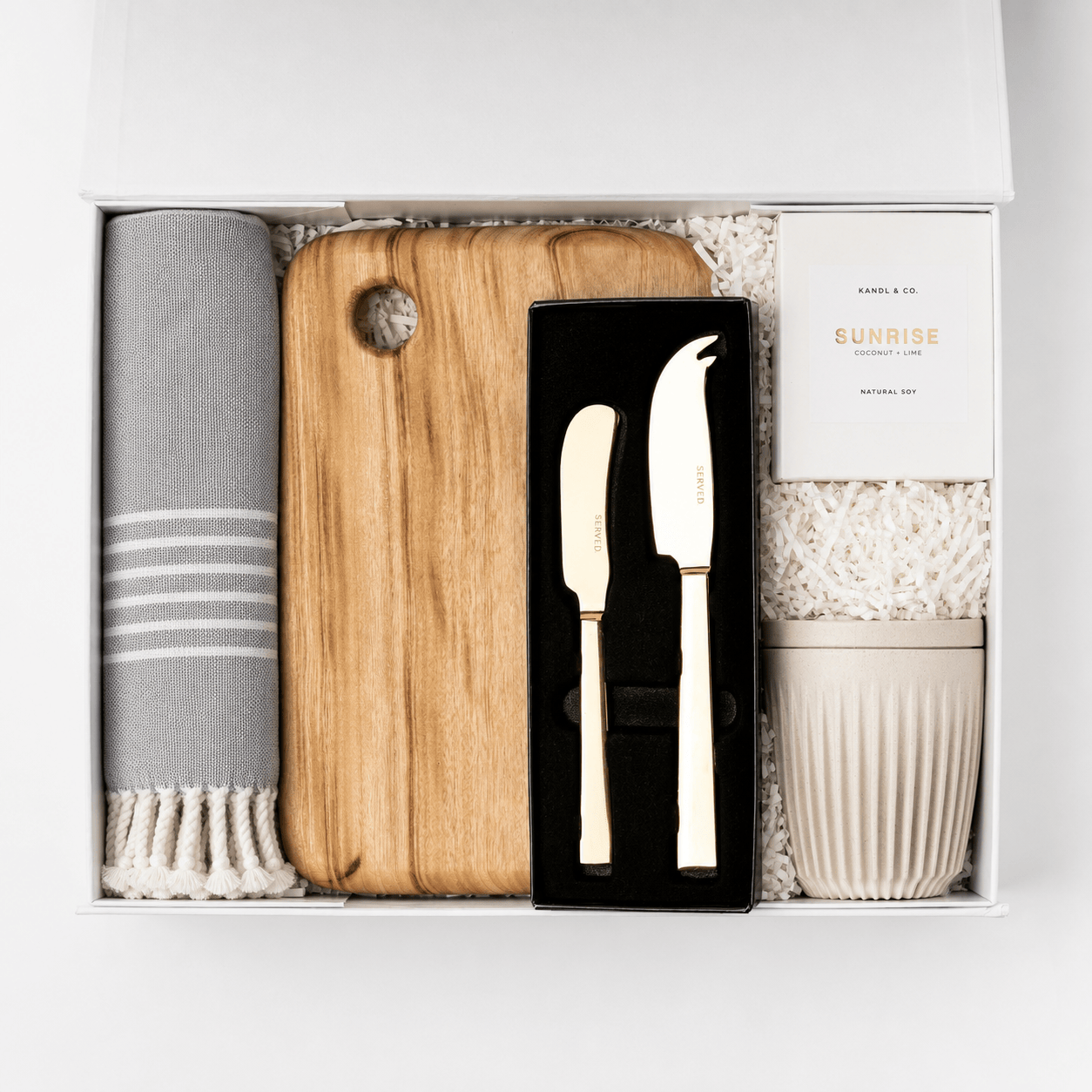 Welcome Home open white gift box containing a rolled grey striped Turkish hand towel, a Camphor Laurel wooden serving board, a SERVED gold cheese and pate knife set, a Kandl & Co candle and a ribbed reusable cup